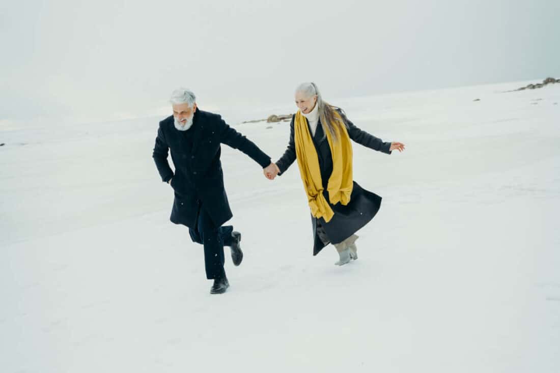 Retired couple holding hands and running in the snow.