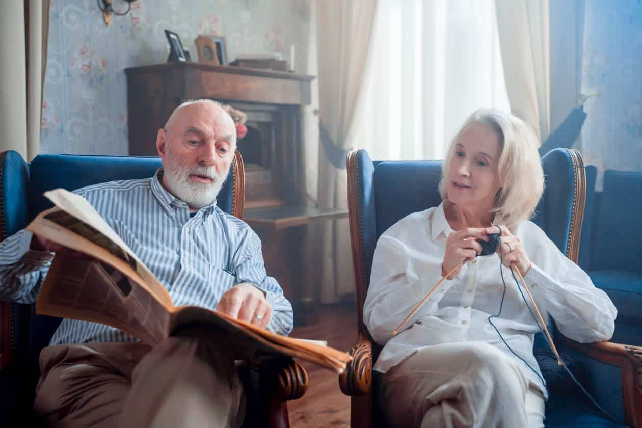 Retired couple reading the newspaper and knitting together.