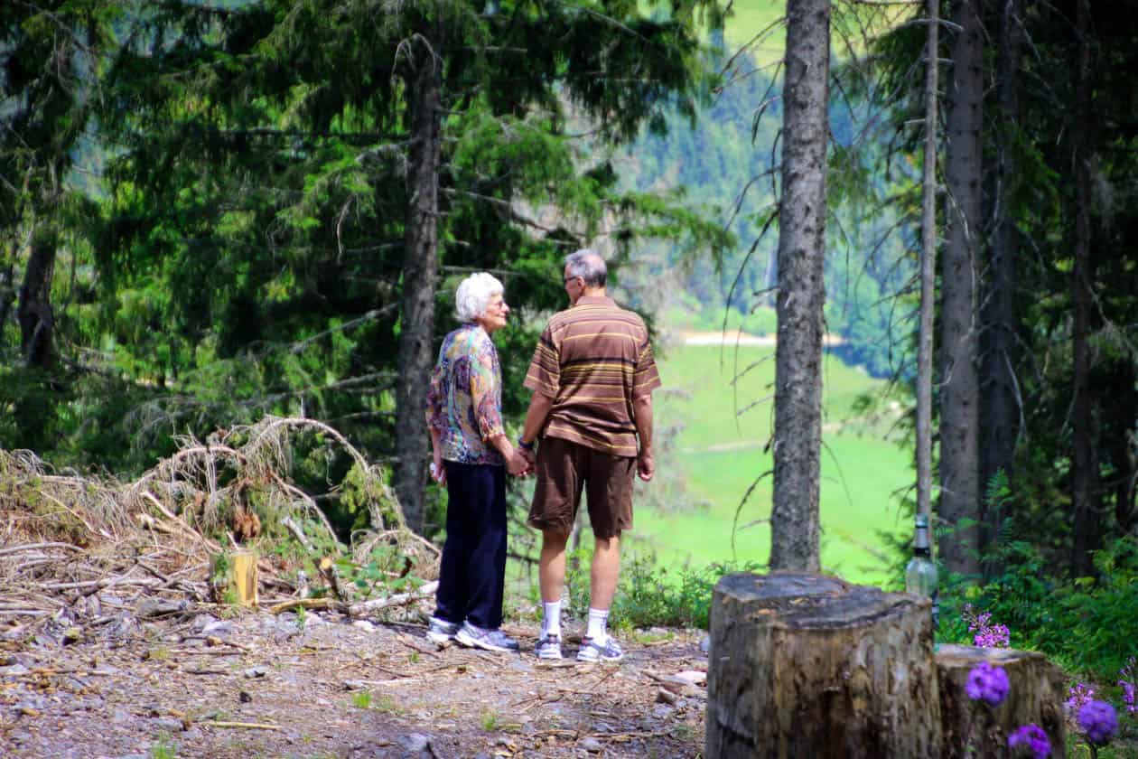 Retired couple holding hands while walking in the woods.